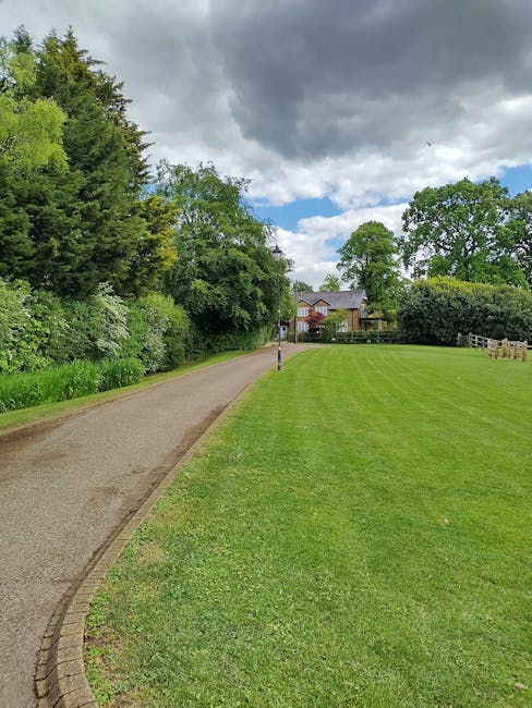 A curved gravel pathway winds through a well-maintained front garden in Lampton Park, bordered by lush, neatly trimmed green grass and edged with white garden edging. On either side of the path, dense